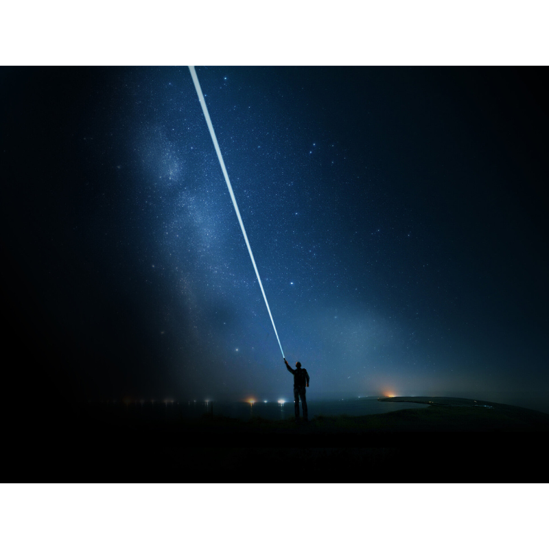 Ein Mensch steht in einer dunklen Nacht unter dem Sternenhimmel und richtet einen extrem starken Lichtstrahl mit der Ledlenser P9R Signature in den Himmel. Die beeindruckende Reichweite der Taschenlampe erhellt die Nacht und zeigt ihre hohe Leuchtkraft. Ideal für Outdoor-Abenteuer, Rettungseinsätze und professionelle Anwendungen.